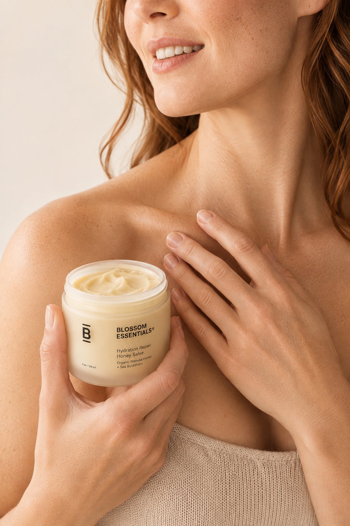 A woman holding a jar of Blossom Essentials Honey Butter cream against a soft beige background.